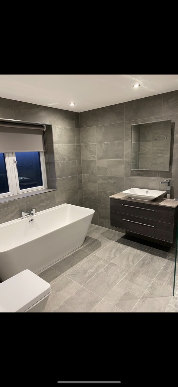Grey tiled bathroom renovation with bath, vanity basin and glass shower screen